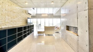 A modern lobby with a stone wall, a sofa, and a flat-screen TV. - Guest House Karst (Motobu)