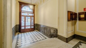 Un couloir avec un sol à motifs, une porte en bois et un lustre.