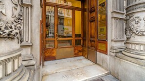 Une entrée d’immeuble ornée de colonnes décoratives, une porte en bois et un panneau indiquant le comptoir d’enregistrement.