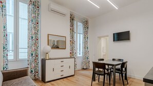 Un salon moderne comprenant un canapé, une table à manger avec des chaises, un téléviseur fixé au mur et un meuble avec des tiroirs.