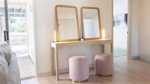 A room with a white console table, two mirrors, and two pink ottomans. - The Wren House (Wilmington Island)