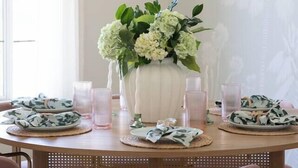 A round dining table with a white vase of flowers, pink glasses, and patterned placemats. - The Wren House (Wilmington Island)