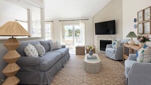 A spacious living room with a grey sofa, a round coffee table, and a fireplace. - The Wren House (Wilmington Island)