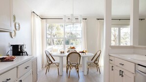 A bright kitchen with white cabinets, a dining table with four chairs, and a coffee machine. - The Wren House (Wilmington Island)