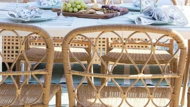 An outdoor dining area with wicker chairs and a table set with plates, glasses, and a fruit basket. - The Wren House (Wilmington Island)