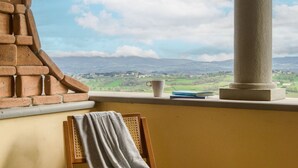 A room with a view of a landscape, a window sill with a cup and book, and a chair with a towel. - Cosy and roomy apartment of 110 sqm for 6 persons on the 1st floor of a rustic-style farmhouse (NO lift or stairs for access), immersed in the Umbrian countryside.The accommodation consists of a kitchen, a living room, three bedrooms, two bathrooms and t (Castiglione del Lago)