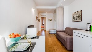 Uma sala de estar moderna com um sofá, uma mesa de jantar posta com pratos e copos, uma tigela de frutas e um quadro na parede.