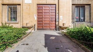 Um edifício com uma grande porta dupla de madeira, uma placa acima da porta e um portão em frente.