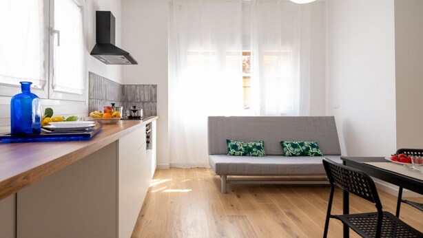 Une cuisine moderne avec un plan de travail en bois, un vase bleu et un coin repas comprenant un canapé gris et des chaises noires.