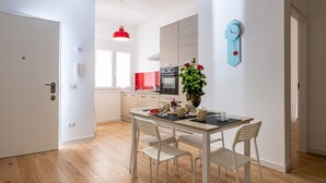 A modern kitchen with a red pendant light, a clock, and a dining area with a table and chairs. - GuestHost - Cozy 55 sqm apartment, for 4 people, located on the ground floor of a modern building. The property is located in a strategic area of ​​Piombino, an ideal starting point for exploring the city and the Tuscan coast. A few minutes from the  (Piombino)