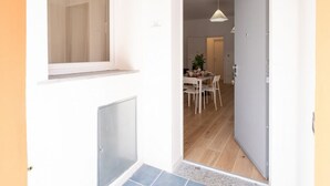 A doorway leading to a dining area with a table and chairs, a hanging light fixture, and a door with a handle. - GuestHost - Cozy 55 sqm apartment, for 4 people, located on the ground floor of a modern building. The property is located in a strategic area of ​​Piombino, an ideal starting point for exploring the city and the Tuscan coast. A few minutes from the  (Piombino)