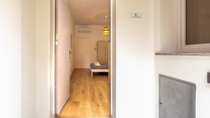 A narrow hallway with a wooden floor, a bed with a blue mattress, and a hanging lamp. - GuestHost - Cozy 40 sqm studio, for 4 people, located on the ground floor of a modern building. The property is located in a strategic area of ​​Piombino, an ideal starting point for exploring the city and the Tuscan coast. A few minutes from the his (Piombino)