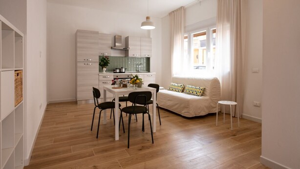 A modern kitchen with white cabinets, a dining table with chairs, and a sofa with a small table. - GuestHost - Cozy 40 sqm studio, for 4 people, located on the ground floor of a modern building. The property is located in a strategic area of ​​Piombino, an ideal starting point for exploring the city and the Tuscan coast. A few minutes from the his (Piombino)