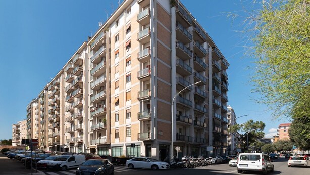 A multi-story residential building with balconies, parked cars, and a clear sky. - GuestHost - Bright apartment of about 100 sqm, perfect for 3 people, located on the seventh floor of a building with elevator (NOT suitable for disabled people - some steps to access it).The property is located in a quiet residential area well connected  (Rome)