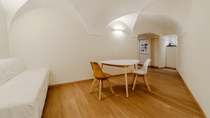 A room with a white sofa, a round table with two chairs, wooden flooring, and a kitchen area in the background. - GuestHost - 80 sqm apartment for 3 people, located on the ground floor (steps required for access). Just a 6-minute drive from Caprafico Beach, the accommodation is in Nervi, one of the most charming districts of Genoa, known for its parks, historic vill (Genova)