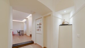 A hallway with a wooden floor, a small table with chairs, a door with a poster, and a statue on a shelf. - GuestHost - 80 sqm apartment for 3 people, located on the ground floor (steps required for access). Just a 6-minute drive from Caprafico Beach, the accommodation is in Nervi, one of the most charming districts of Genoa, known for its parks, historic vill (Genova)