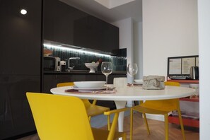 A modern dining area with a white table, yellow chairs, and a kitchen in the background.