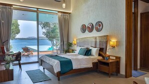 Une chambre avec un grand lit, un bureau et une chaise, une table de chevet et une vue sur la mer.