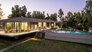 Une maison moderne dotée d’un patio entièrement vitré, d’une piscine et d’une terrasse offrant une vue sur un plan d’eau.