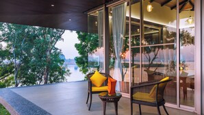 Un espace extérieur aménagé avec des chaises et des coussins en osier, une table en verre et une vue sur des arbres et une étendue d’eau.