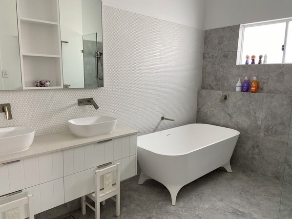 Un baño moderno con una bañera independiente, un espejo grande y un tocador con lavabo blanco.