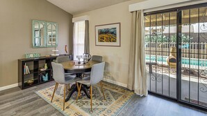 A dining area with a round table, four gray chairs, a patterned rug, a bookshelf, a framed picture, and a sliding glass door leading to an outdoor area with a pool. - 'Coyote Casa' w/ Mtn Views in Tuscon Desert Oasis (Tucson)