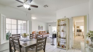 A spacious dining area with a wooden table and chairs, a ceiling fan, and a view to the living room.