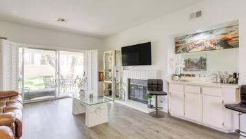 A modern living room with a glass coffee table, a fireplace, a TV mounted on the wall, and a dining area with chairs.