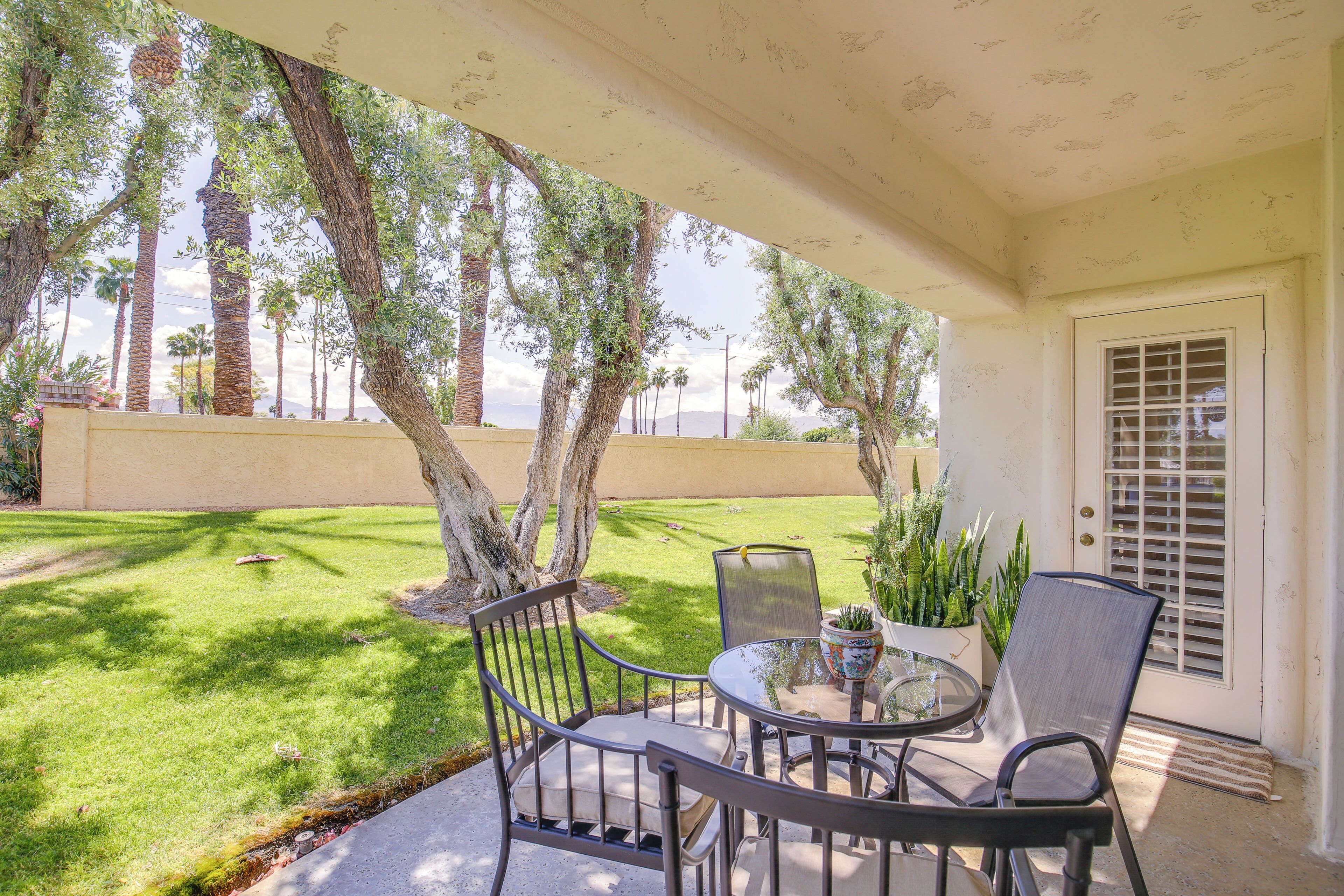 An outdoor patio with a table and chairs, surrounded by palm trees and a well-maintained lawn.