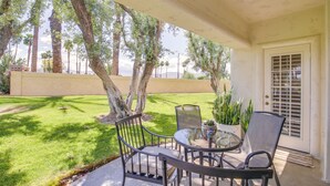 An outdoor patio with a table and chairs, surrounded by palm trees and a well-maintained lawn.