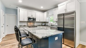 A modern kitchen with white cabinets, a stainless steel refrigerator, a granite countertop, and a bar stool. - Walk to Beach & Harbor: Dtwn Pass Christian Home (Pass Christian)