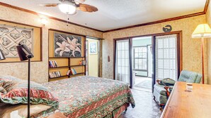 Ein Schlafzimmer mit Bett, Schreibtisch, Stuhl, Bücherregal, Deckenventilator und Blick durch eine Glastür.