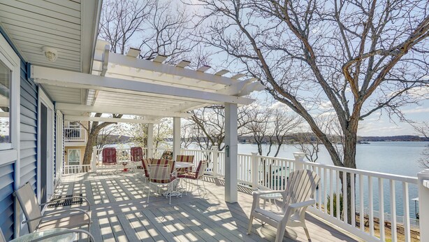 Una terraza techada con mobiliario exterior, un pérgola y vistas a un lago.