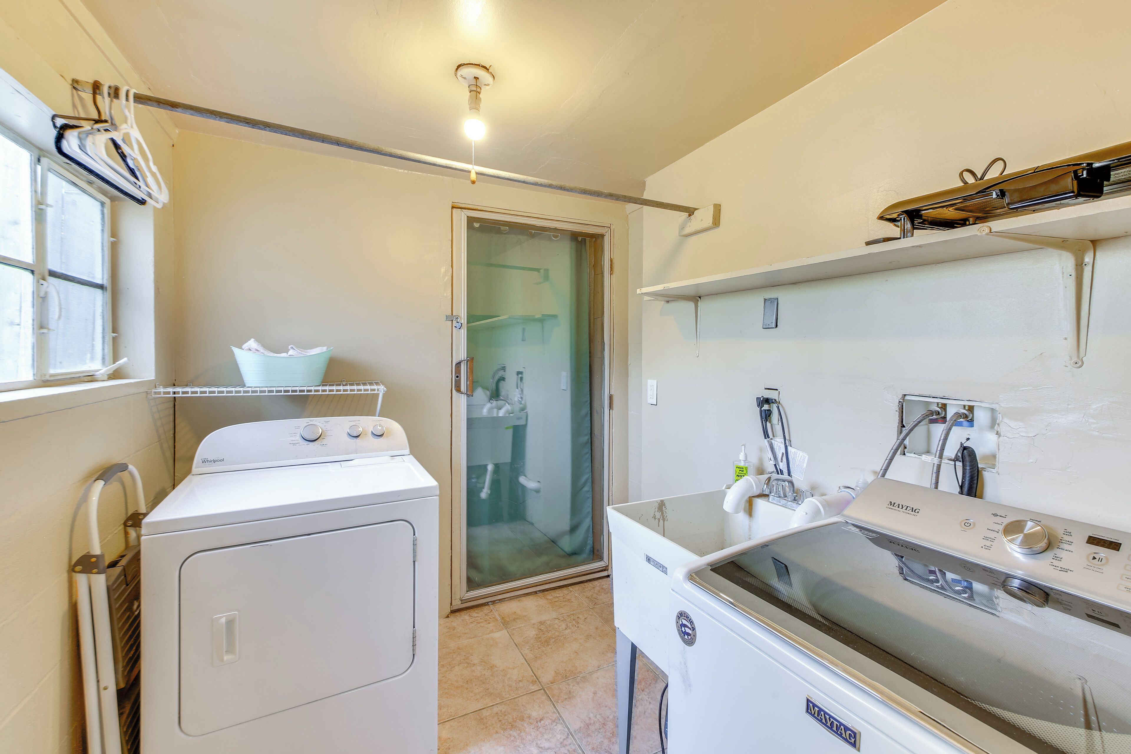 A laundry room with a front-loading washer and dryer, a glass shower door, and a ceiling light fixture.