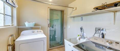 A laundry room with a front-loading washer and dryer, a glass shower door, and a ceiling light fixture.