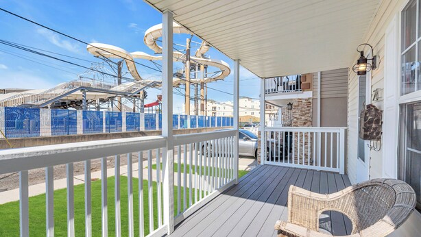 A covered porch with a white railing, a wicker chair, and a view of a water slide structure in the background.