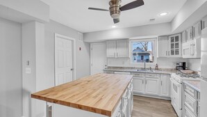 A modern kitchen with white cabinetry, a wooden island, and a ceiling fan.