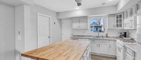 A modern kitchen with white cabinetry, a wooden island, and a ceiling fan.