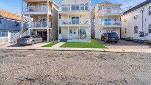 A multi-story residential building with a central balcony, a garage, and a driveway with two cars parked.