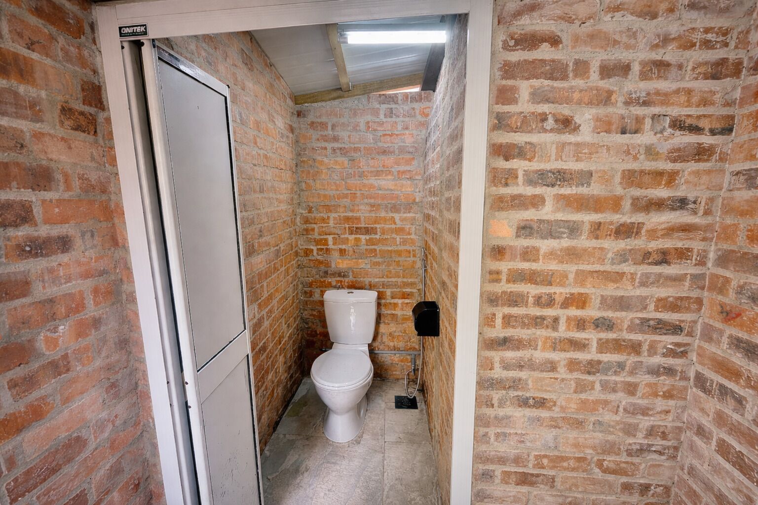 Un baño estrecho con paredes de ladrillo, un inodoro blanco y un calentador de agua a la vista.