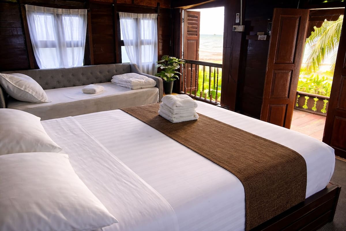 Quarto de hotel com duas camas, varanda e vista para a praia, além de um vaso de plantas.