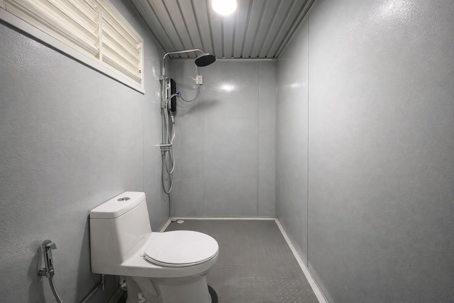 Un baño pequeño y estrecho con inodoro, ducha y ventana con persianas.