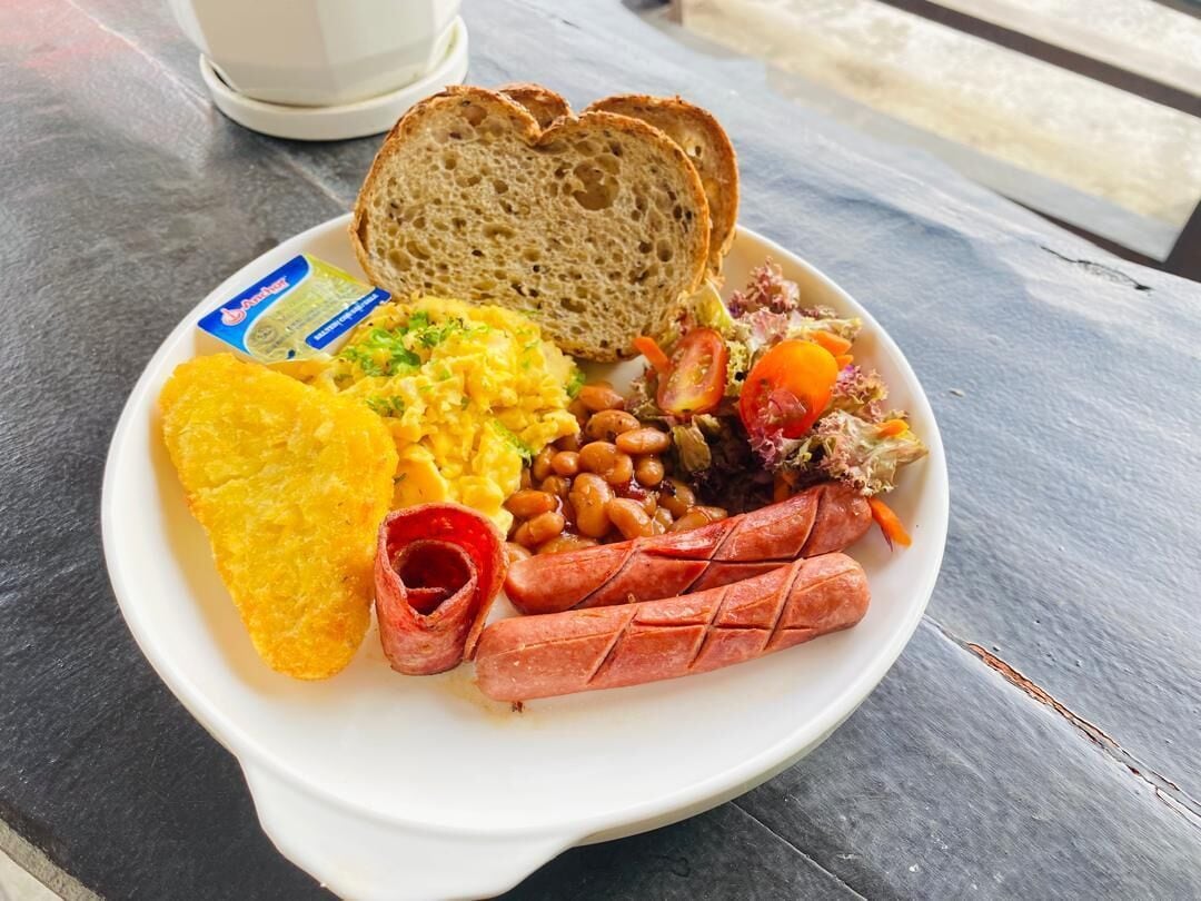 A plate of food including scrambled eggs, beans, sausages, and toast on a table.
