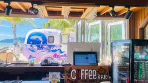 Un bar de café con vistas tropicales, una caja registradora y un refrigerador.