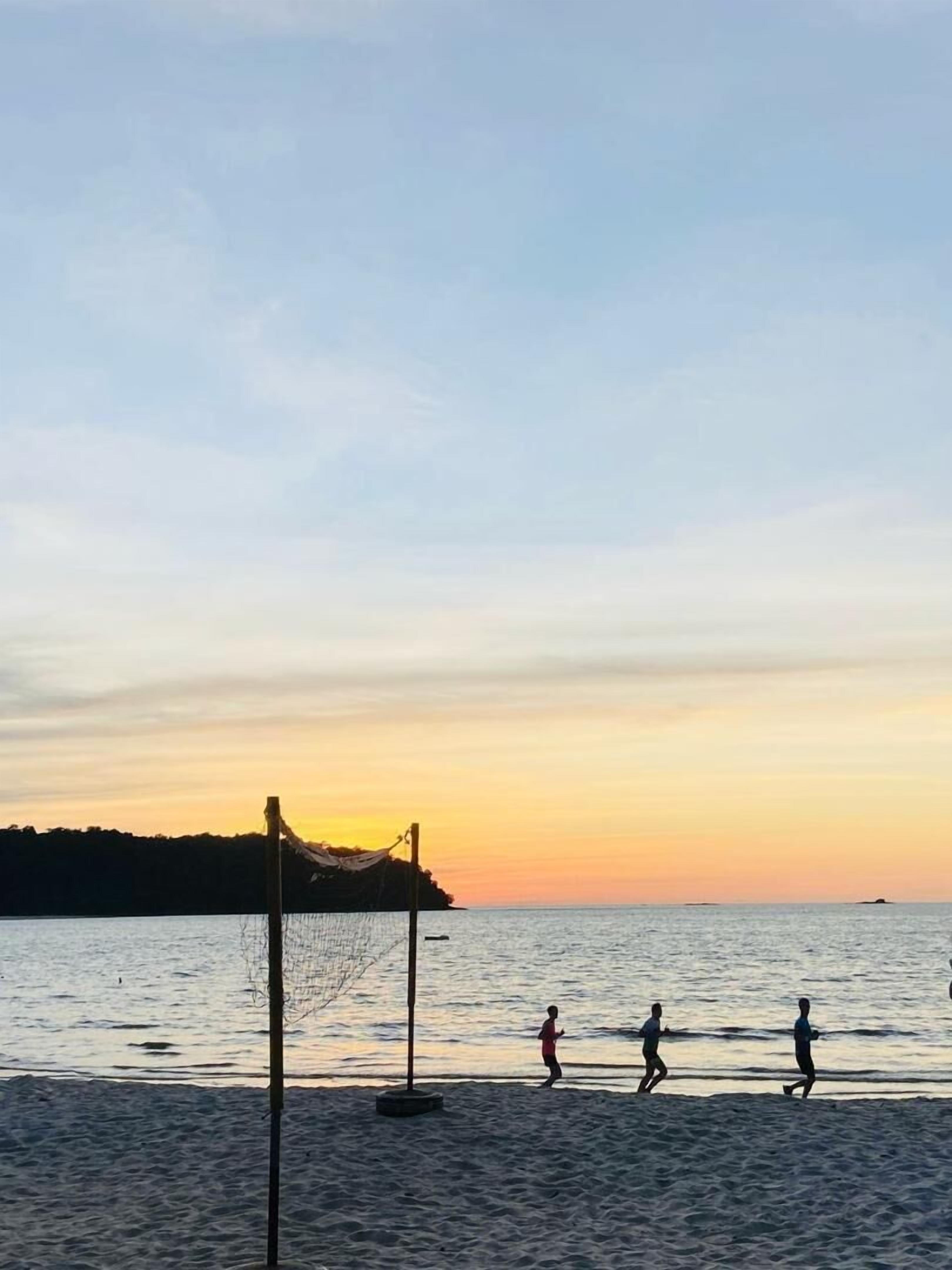 A beach scene with a volleyball net and people playing.