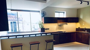 A modern kitchen with a large window, dark wooden cabinets, a white tiled backsplash, and three bar stools. - Hidden Negombo by Sana's (Negombo)