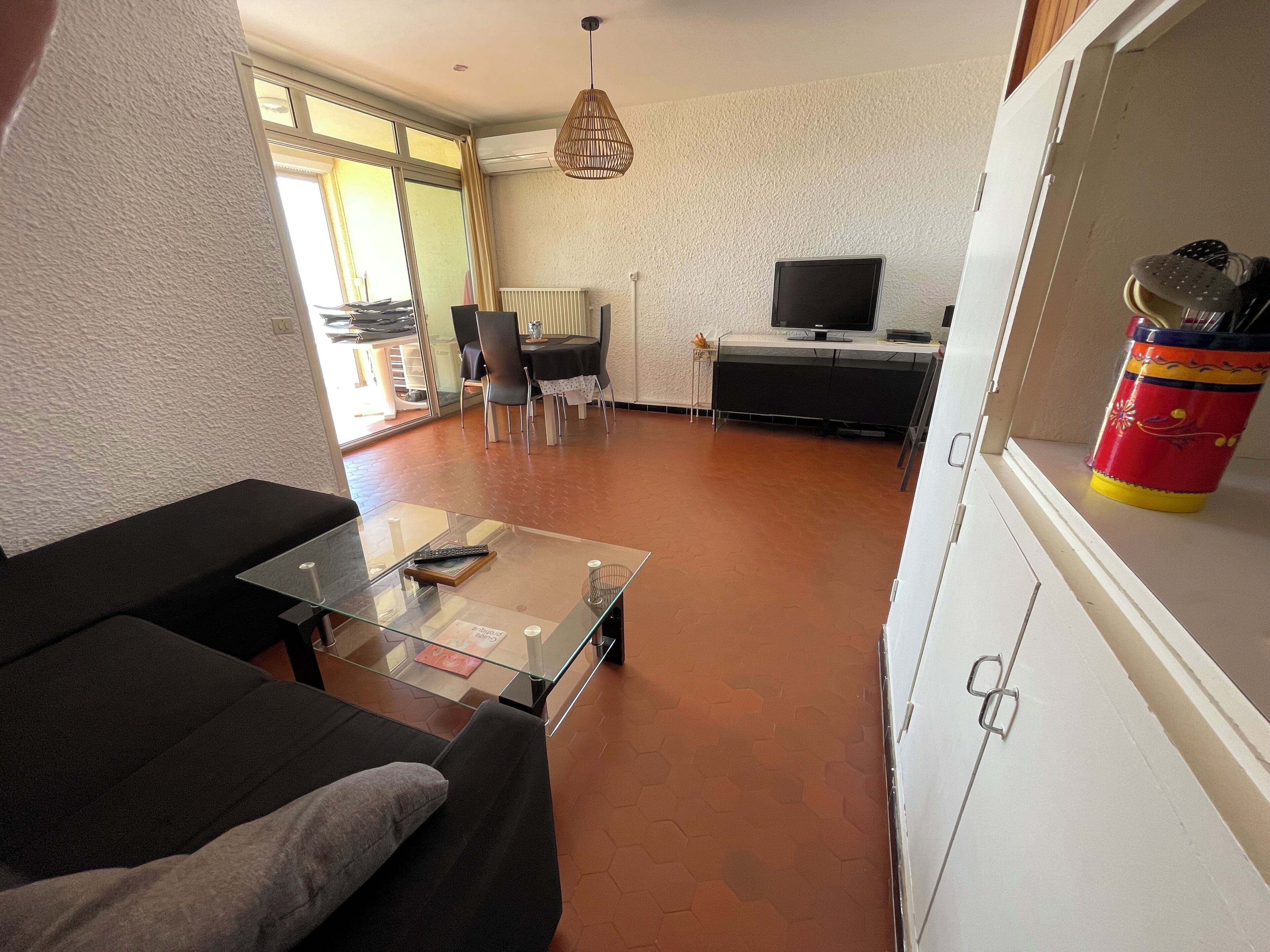 Un salon comprenant une table basse en verre, un canapé, un téléviseur posé sur un meuble et un coin repas avec des chaises et une table.