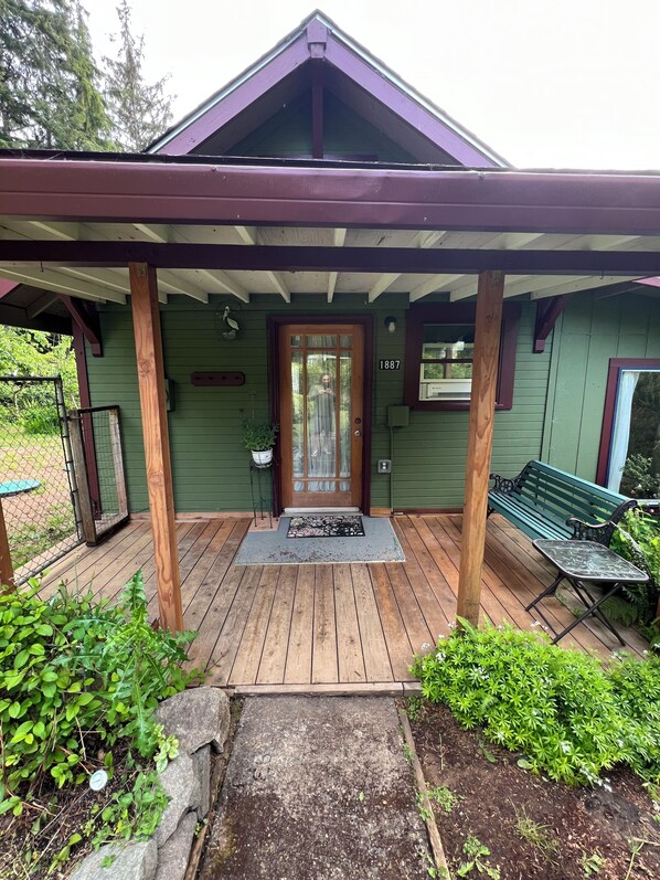 A green house with a wooden porch, a door with a glass panel, and a number '1887' on the wall.