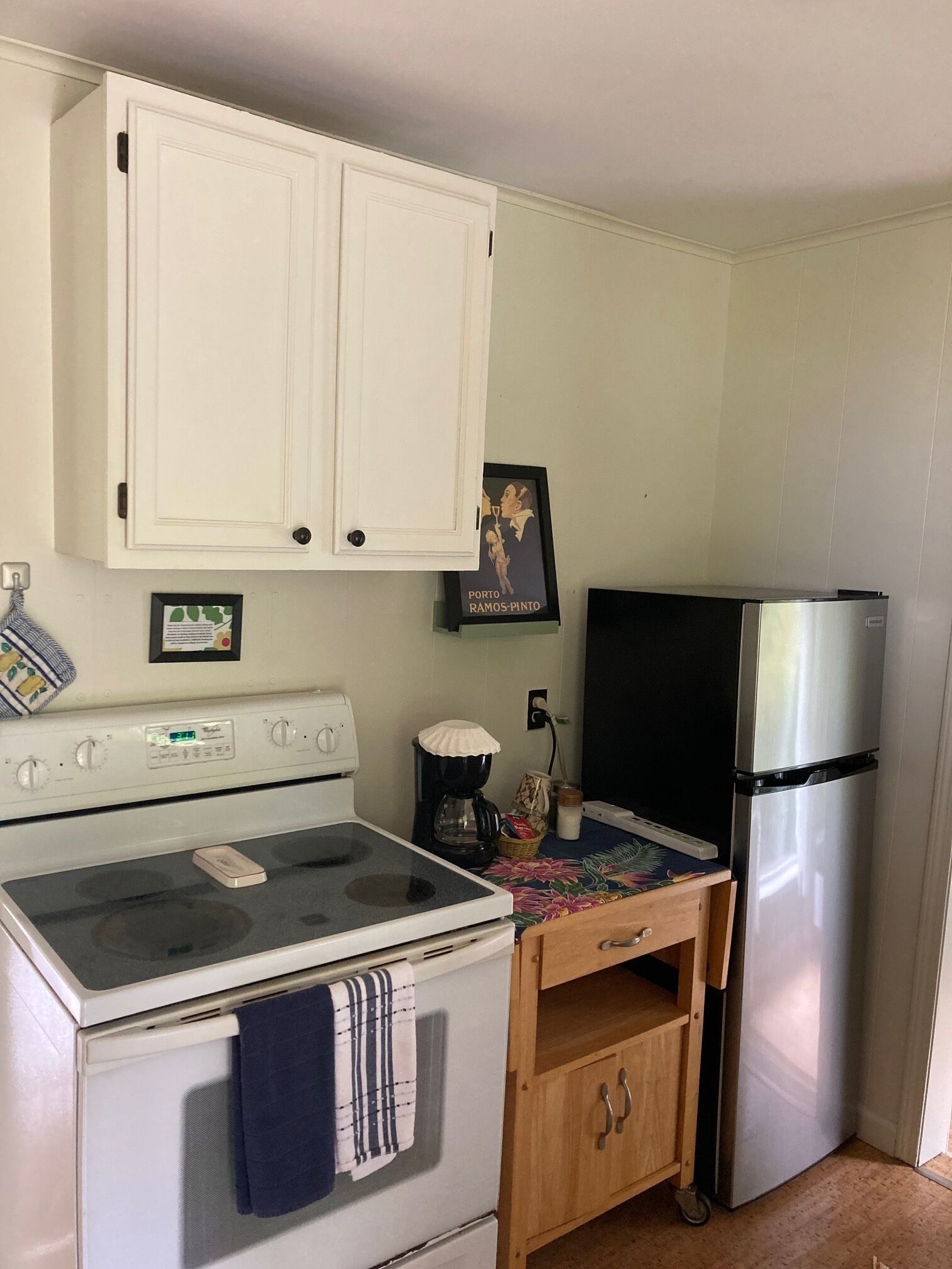 Una cocina con gabinetes blancos, estufa, cafetera y refrigerador.