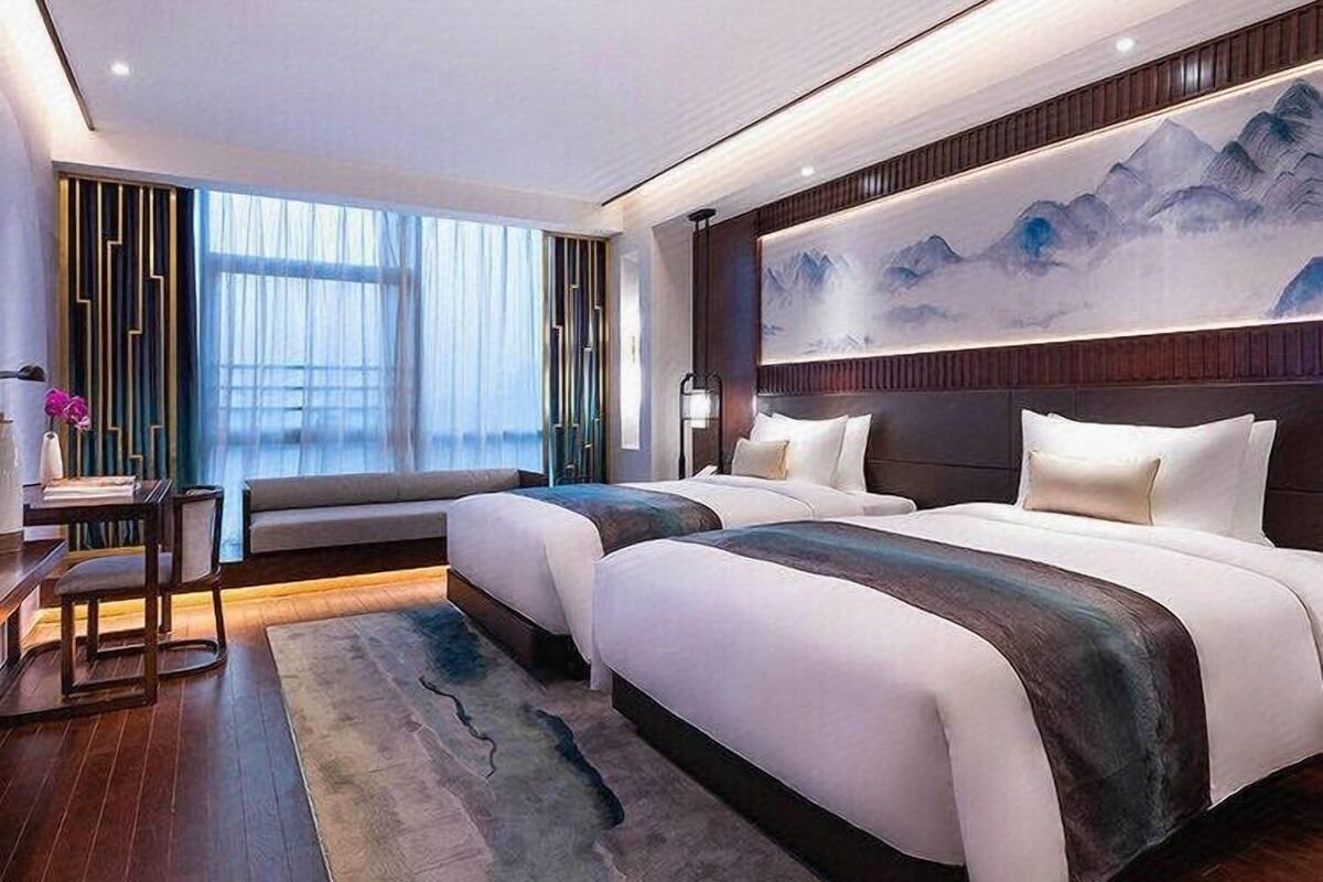 A modern hotel room with a large bed, a seating area, and a view of the mountains.